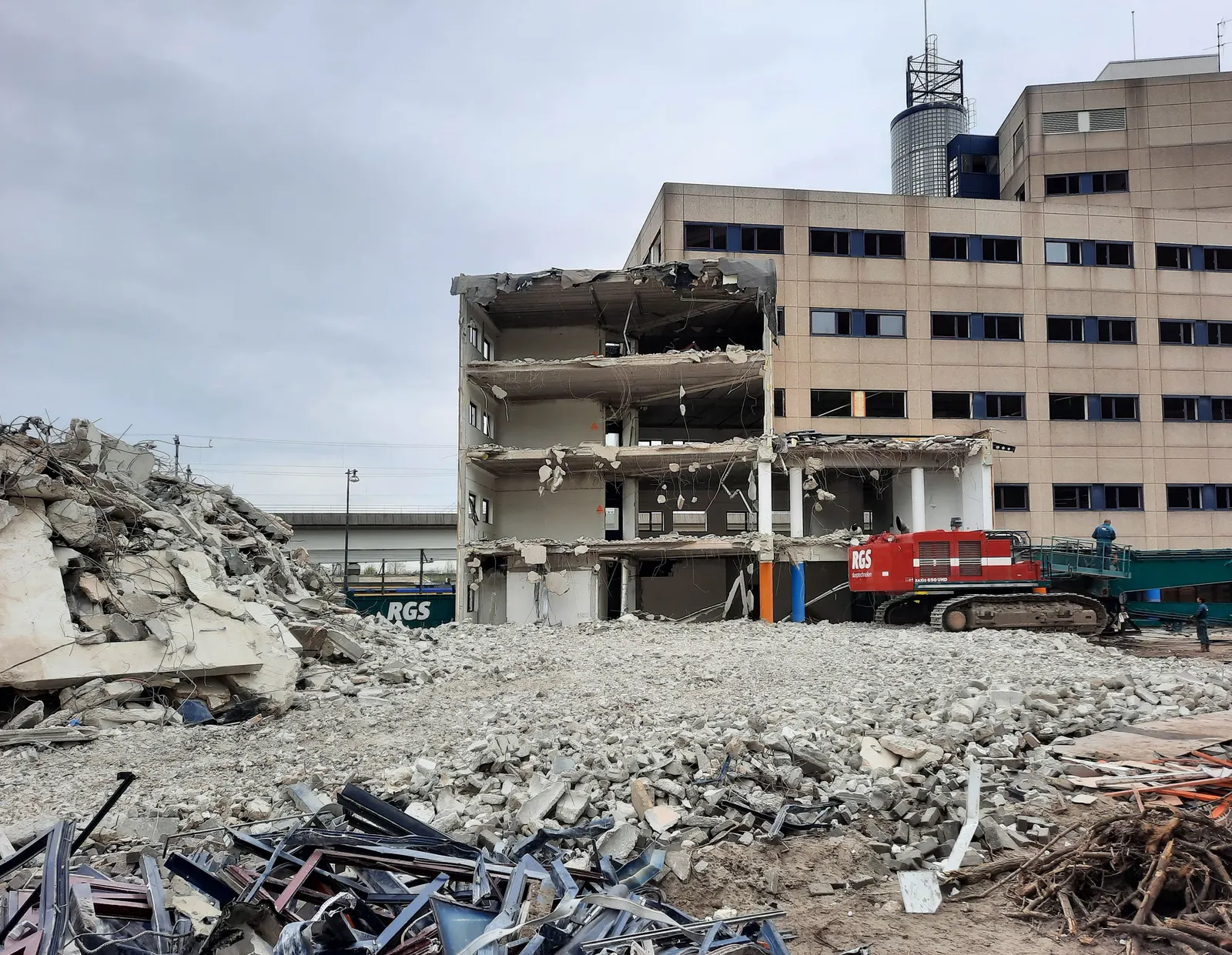 Office block partly demolished, with a demolition excavator and piles of concrete and metal debris