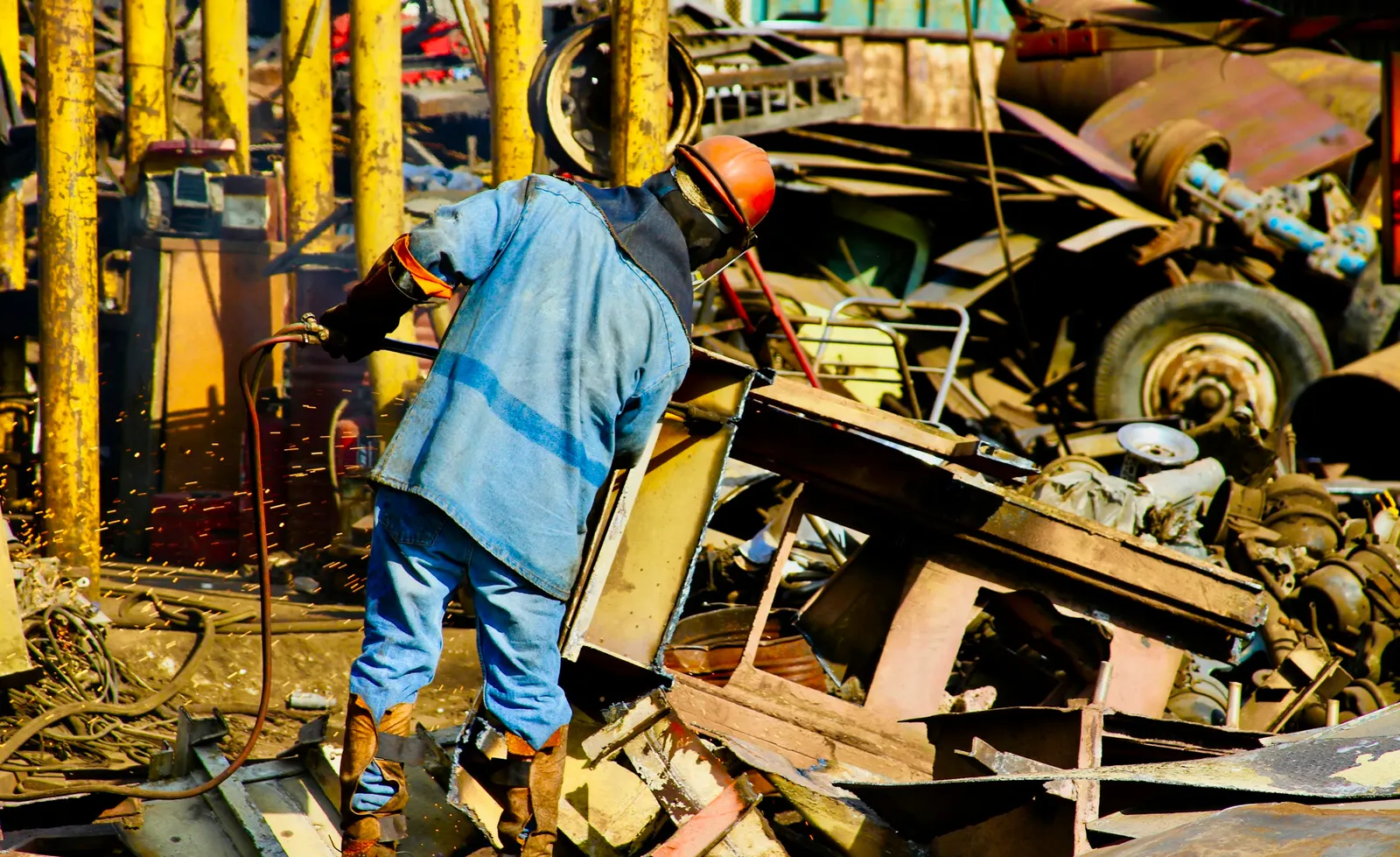 Worker in a hard hat cutting scrap metal in a yard